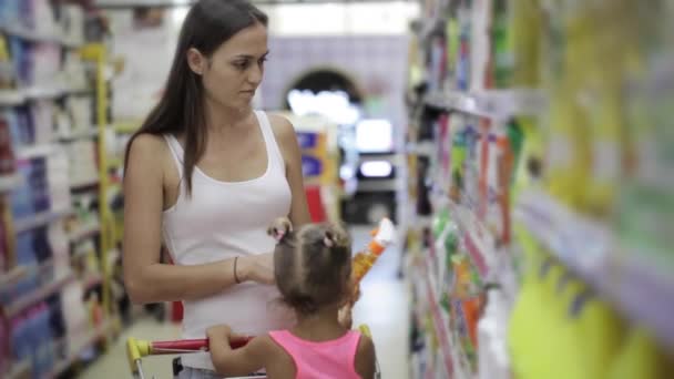 Mujeres jóvenes con hija pequeña seleccionando detergentes para la casa en el supermercado — Vídeo de stock