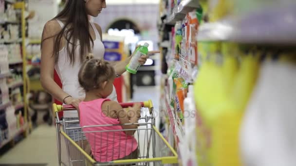 Mujeres jóvenes con hija pequeña seleccionando detergentes para la casa en el supermercado — Vídeo de stock