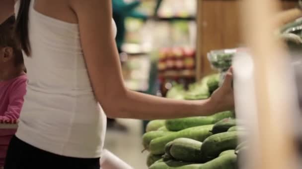 Família jovem de mãe e filha pequena escolhendo legumes no supermercado . — Vídeo de Stock
