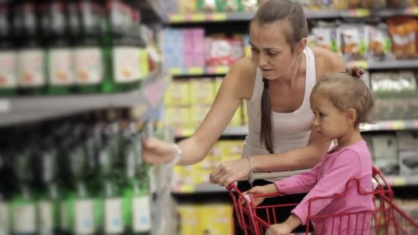 Attraktive junge Frau mit kleiner Tochter bei der Getränkeauswahl im Supermarkt. — Stockvideo