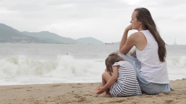 Mutter mit Tochter sitzt mit dem Rücken zur Kamera am Sandstrand. — Stockvideo