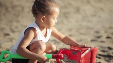 Küçük kırmızı oyuncak kepçe ile oynayan kız ve kumlu plajda kürek