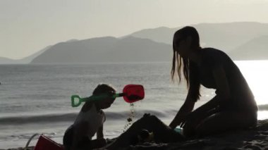 Anne ve küçük kızı kumsalda kumdan kaleler inşa silüeti