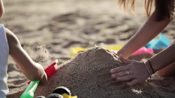 Ung mamma med lilla dotter leker med sand på stranden — Stockvideo