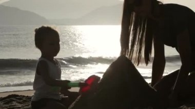 Anne ve küçük kızı kumsalda kumdan kaleler inşa silüeti