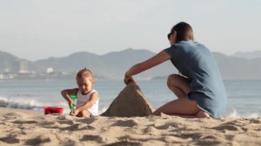 Suya yakın plaj kum üzerinde küçük kızı ile oynarken annesi