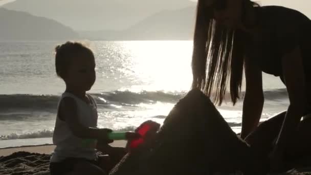 Силуэт матери и маленькой дочери, строящих песчаные замки на пляже — стоковое видео