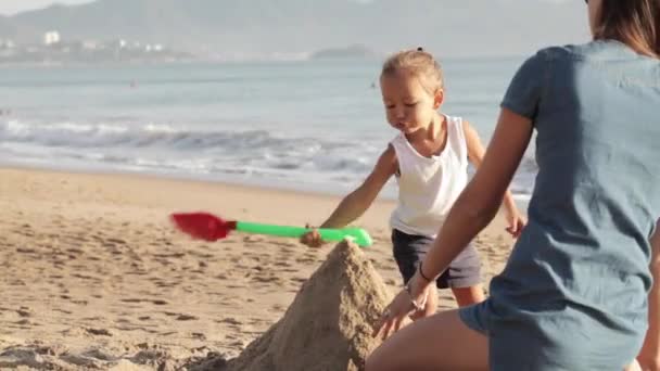 Madre che gioca con la sua bambina sulla spiaggia vicino all'acqua sulla sabbia — Video Stock