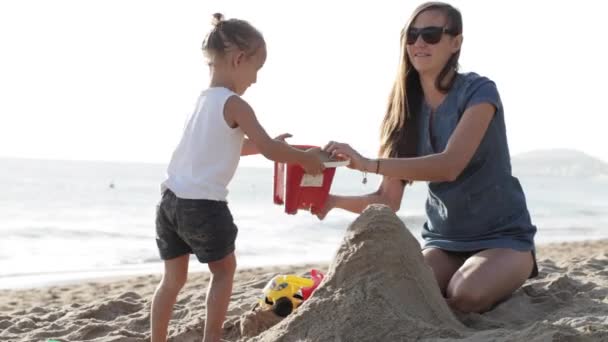 Suya yakın plaj kum üzerinde küçük kızı ile oynarken annesi — Stok video