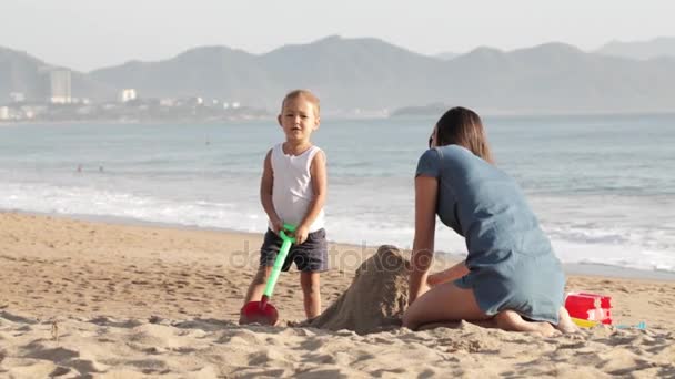Mama gra z jej małą córeczkę na plaży w pobliżu wody, na piasku — Wideo stockowe