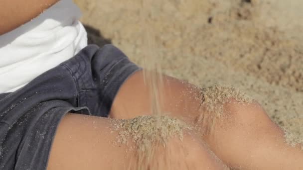 Meisje kind gooit zand op haar benen op het strand — Stockvideo