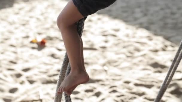 Милая девочка играет и делает гимнастические упражнения на качелях на песчаном пляже — стоковое видео