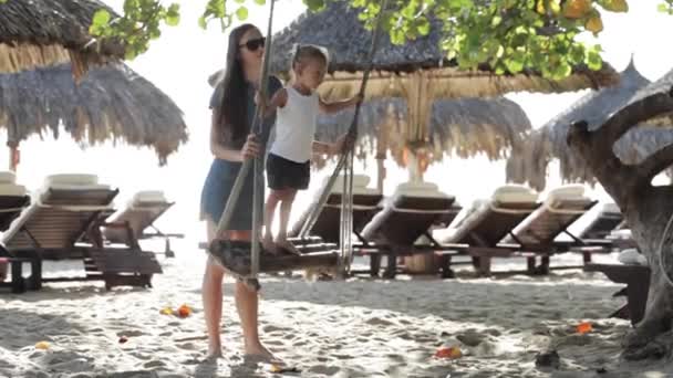 Ung mamma driver söta lilla dotter på swing på sandstranden — Stockvideo