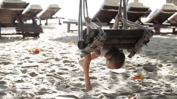 Söt baby flicka spelar och gör gymnastiska utöva på gungan vid sandstrand — Stockvideo