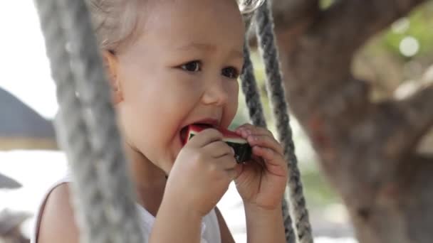 LClose-up de lttle linda niña sentada en el columpio y comer sandía roja . — Vídeo de stock