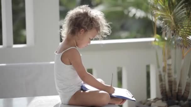 Menina desenhar a lápis sobre o papel na varanda com palmeiras no fundo — Vídeo de Stock