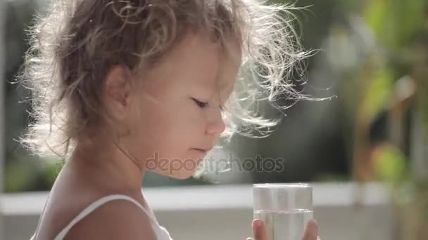 Απαλή πλάνα από χαριτωμένο κοριτσάκι με ηλιοφάνεια στα μαλλιά πίνουν νερό από γυαλί — Αρχείο Βίντεο