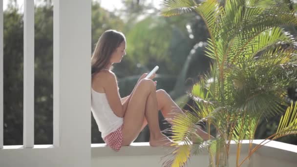 Žena používající smartphone při posezení na terase se zahrádkou na pozadí