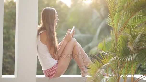 Arka plan üzerinde bahçeli terasta otururken Smartphone kullanan kadın — Stok video