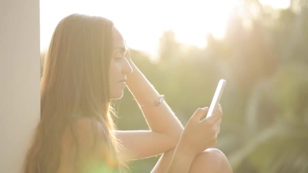 Mujer usando teléfono inteligente mientras está sentado en la terraza con jardín en el fondo — Vídeo de stock