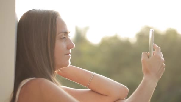 Woman using smartphone while sitting on terrace with garden on background — Stock Video