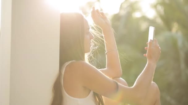 Mujer usando teléfono inteligente mientras está sentado en la terraza con jardín en el fondo — Vídeo de stock