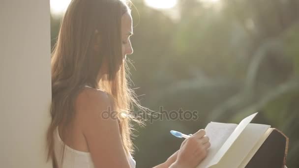 Nő erkély ül, és írásban napló-kert, a háttérben — Stock videók