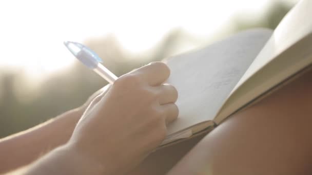 De vrouw zit op balkon en schrijven in dagboek met tuin op de achtergrond — Stockvideo