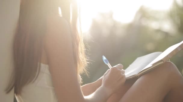 Kobieta siedzi na balkon i pisanie w pamiętnik z ogrodem w tle — Wideo stockowe