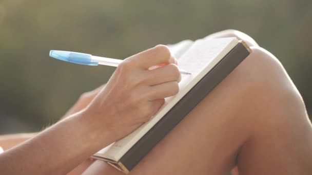 Woman sitting at balcony and writing in diary with garden on the background — Stock Video