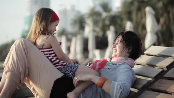 Yong madre con pequeña hija abrazo en la cama solar en la playa de arena — Vídeo de stock