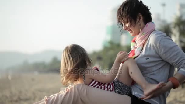 Yong madre con pequeña hija abrazo en la cama solar en la playa de arena — Vídeo de stock