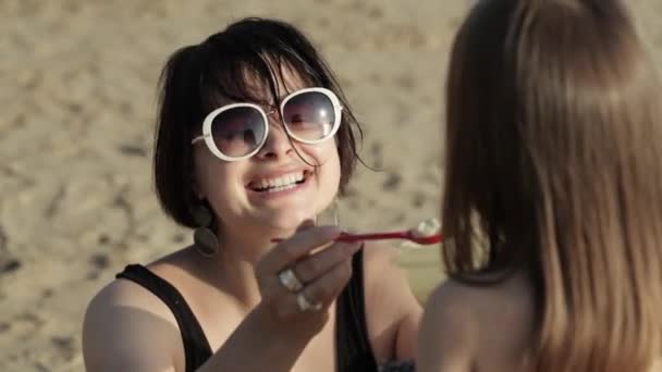 Primer plano de la mujer joven alimentando a su hijita en la playa — Vídeos de Stock
