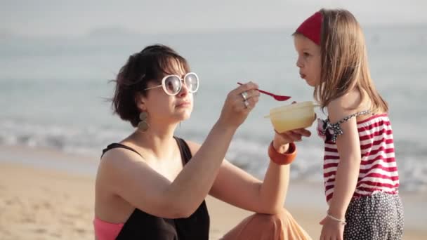 Close-up van jonge vrouw voederen dochtertje op het strand — Stockvideo
