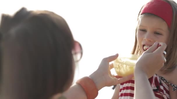 Nahaufnahme einer jungen Frau, die ihre kleine Tochter am Strand füttert — Stockvideo