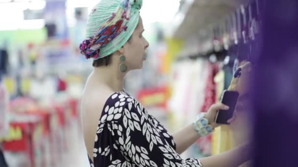 Привлекательная женщина выбирает детскую одежду в супермаркете . — стоковое видео