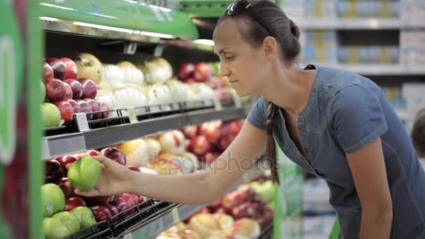 Женщина выбирает свежие яблоки в продуктовом магазине — стоковое видео