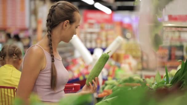 Молодая мама с маленькой дочкой в тележке выбирает зелень в супермаркете — стоковое видео