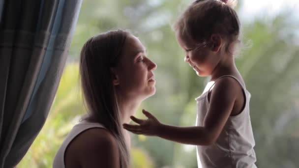 Мать и милая маленькая дочь разговаривают, улыбаются и обнимаются на подоконнике — стоковое видео