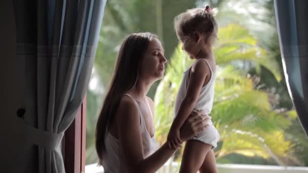 Madre y linda hijita hablando, sonriendo y abrazándose en el alféizar de la ventana — Vídeo de stock