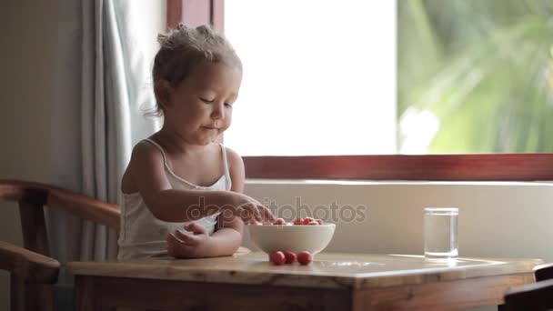 어린 소녀는 테이블 및 체리 토마토를 먹는 앉아 — 비디오