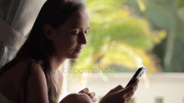 Akıllı telefon evde penceresini kullanarak genç çekici kadın