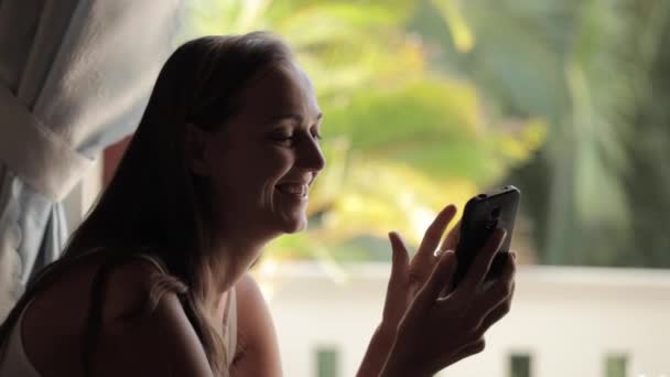 Молодая женщина, используя смартфон и смеясь — стоковое видео