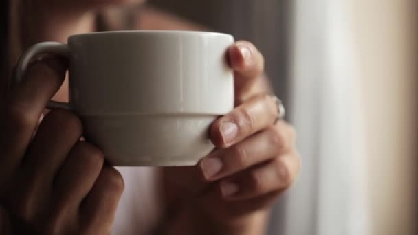 Молодая привлекательная женщина сидит у окна и пьет чай — стоковое видео