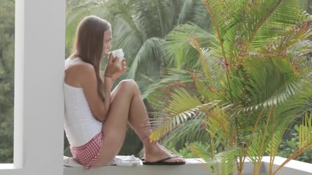 Junge attraktive Frau trinkt Kaffee oder Tee auf dem Balkon, Nahaufnahme — Stockvideo