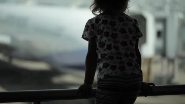 Дитина в аеропорту біля вікна дивиться на літаки і чекає часу польоту — стокове відео