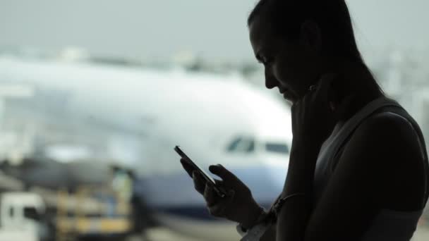 Mujer joven con teléfono inteligente en el aeropuerto con avión en el fondo — Vídeo de stock