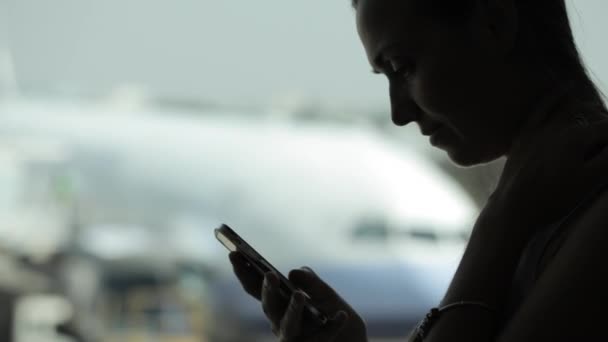 Mujer joven con teléfono inteligente en el aeropuerto con avión en el fondo — Vídeos de Stock