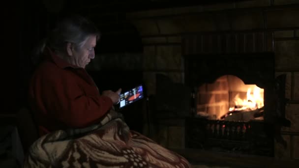 Hombre mayor sentado junto a la chimenea y utilizando la tableta — Vídeos de Stock