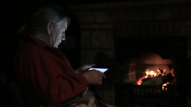 Старший сидит у камина и с помощью планшета — стоковое видео